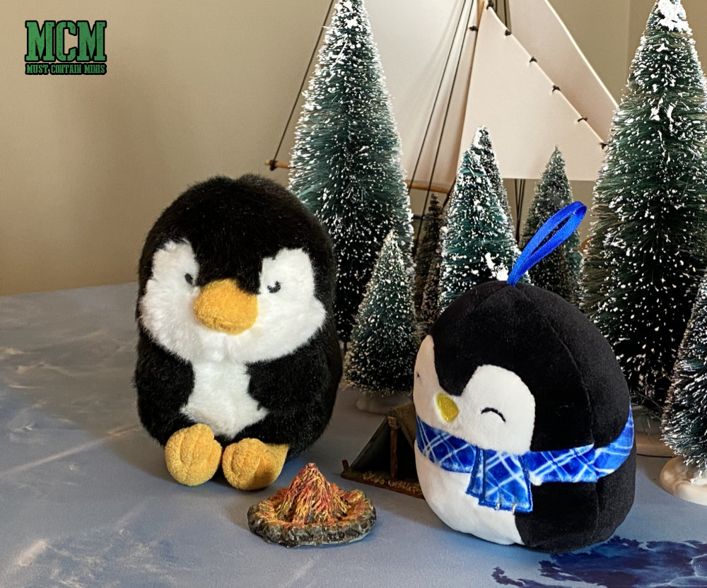 Two stuffie penguins sit around a campfire.